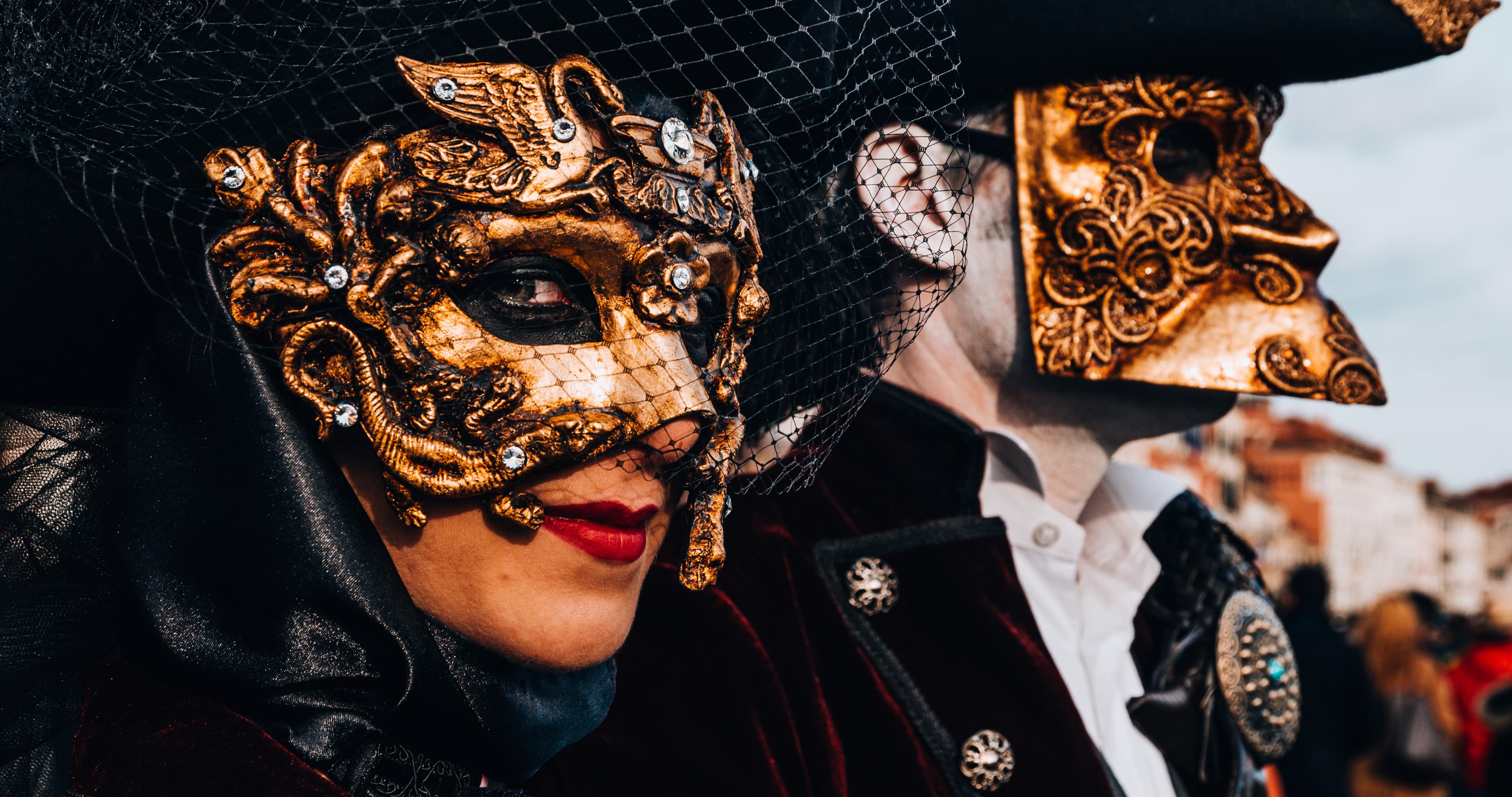 Close-up of a masked couple wearing elegant gold Venetian-style masquerade masks and dramatic black costumes.