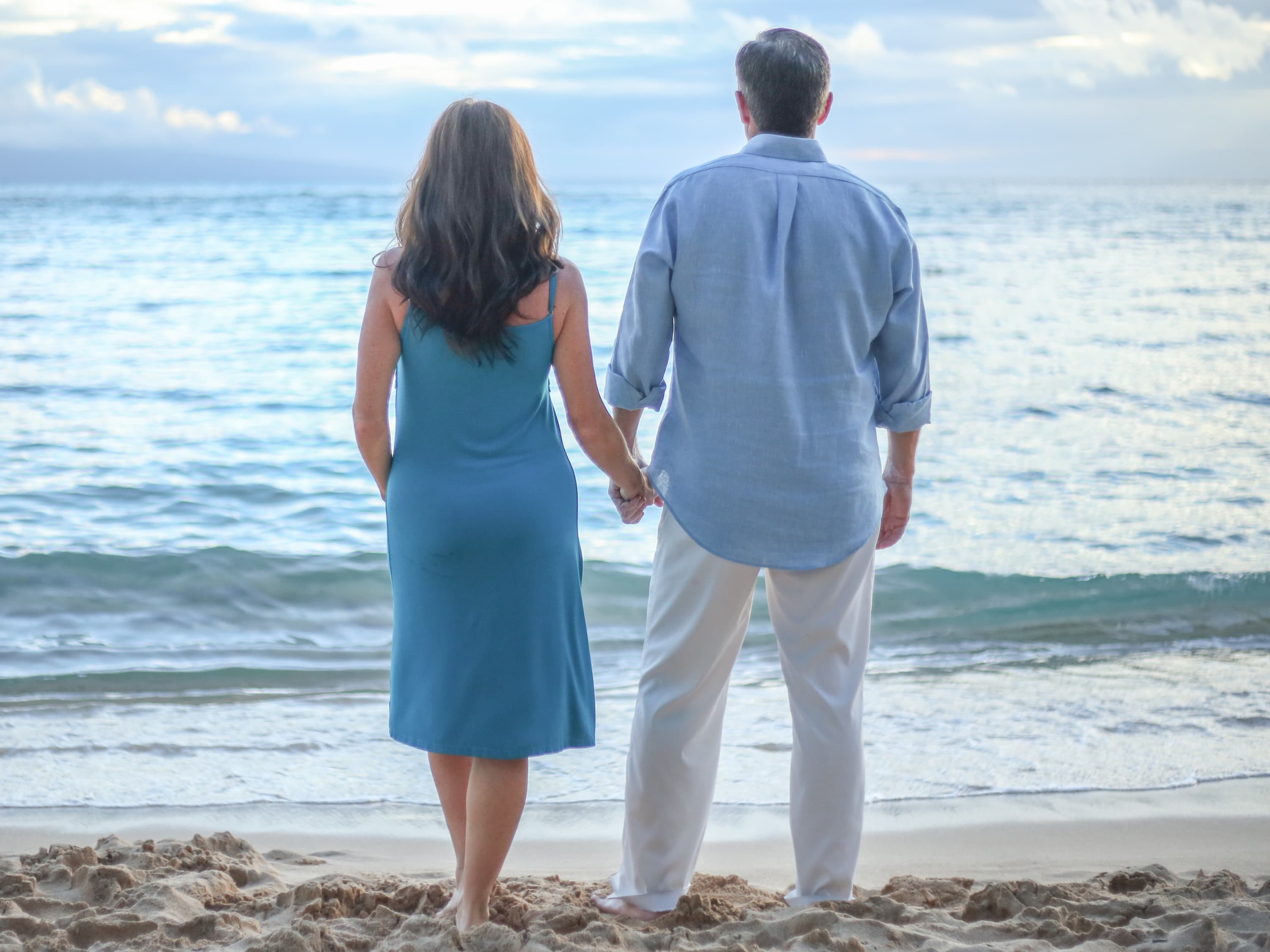 A man and woman holding hands while looking out at the beach, reconnecting after a marriage crisis.