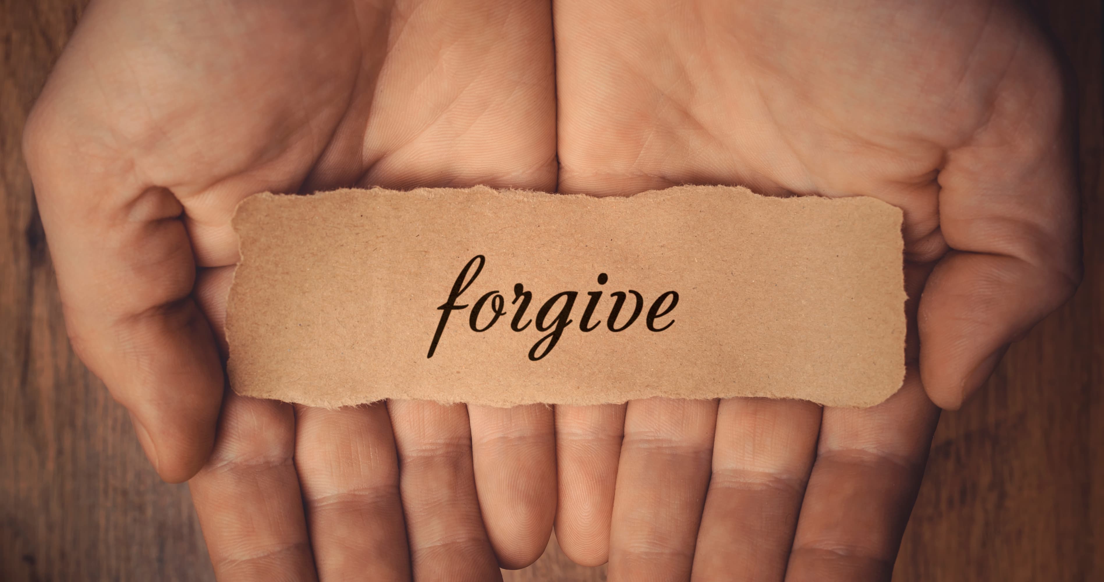 Hands holding a card with the word forgive, symbolizing apology and forgiveness in marriage and healing after relationship conflict.