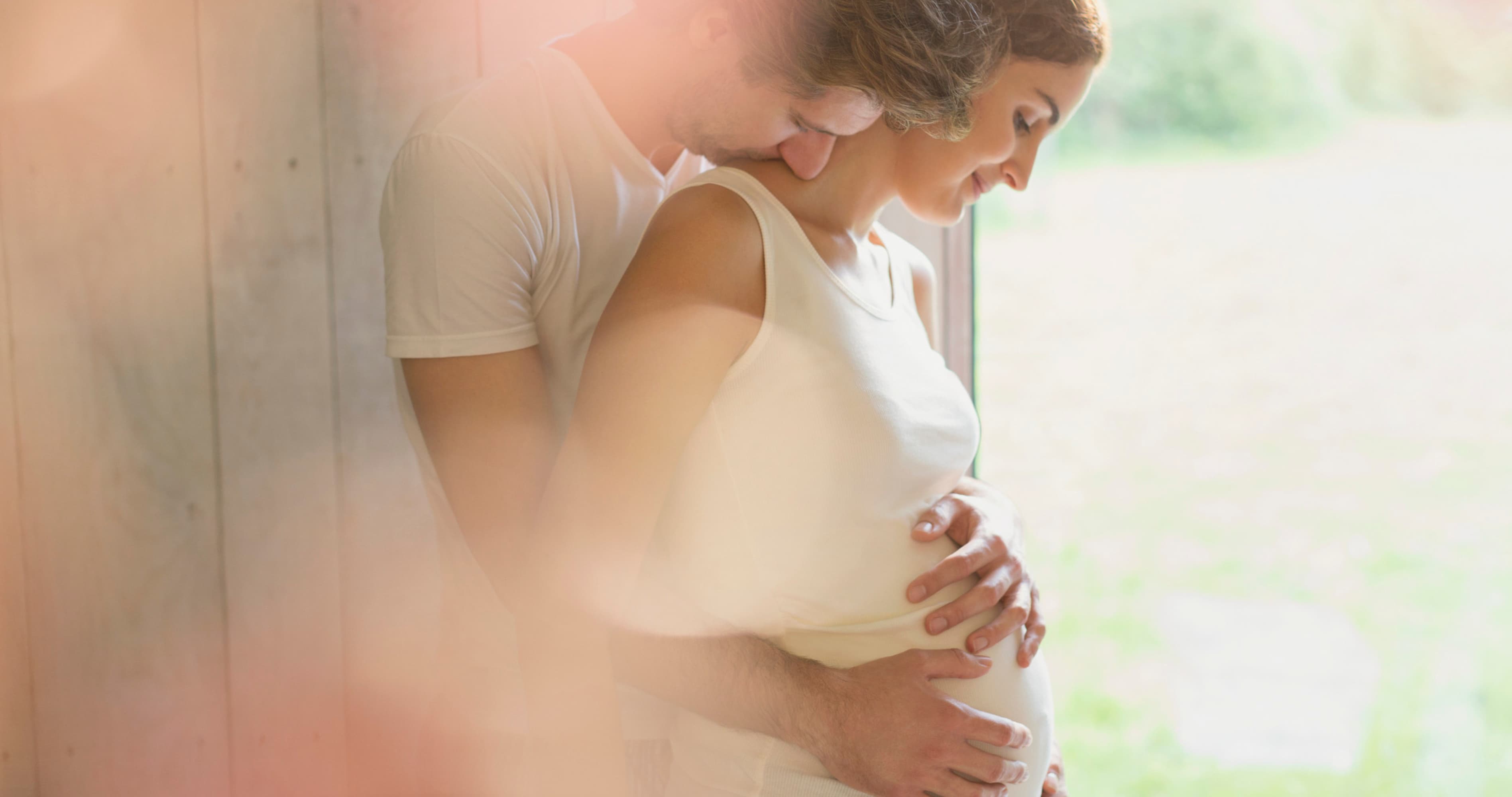 Pregnant woman being lovingly held by her partner, showing emotional security, intimacy, and trust in a relationship.
