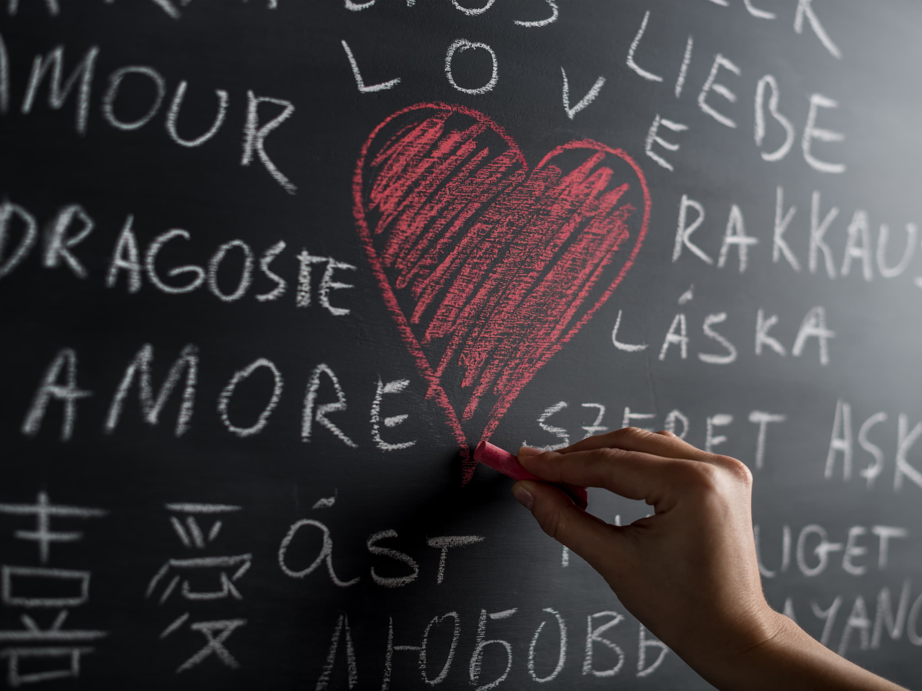 A hand drawing a red heart with chalk on a blackboard, representing rebuilding communication in a marriage.