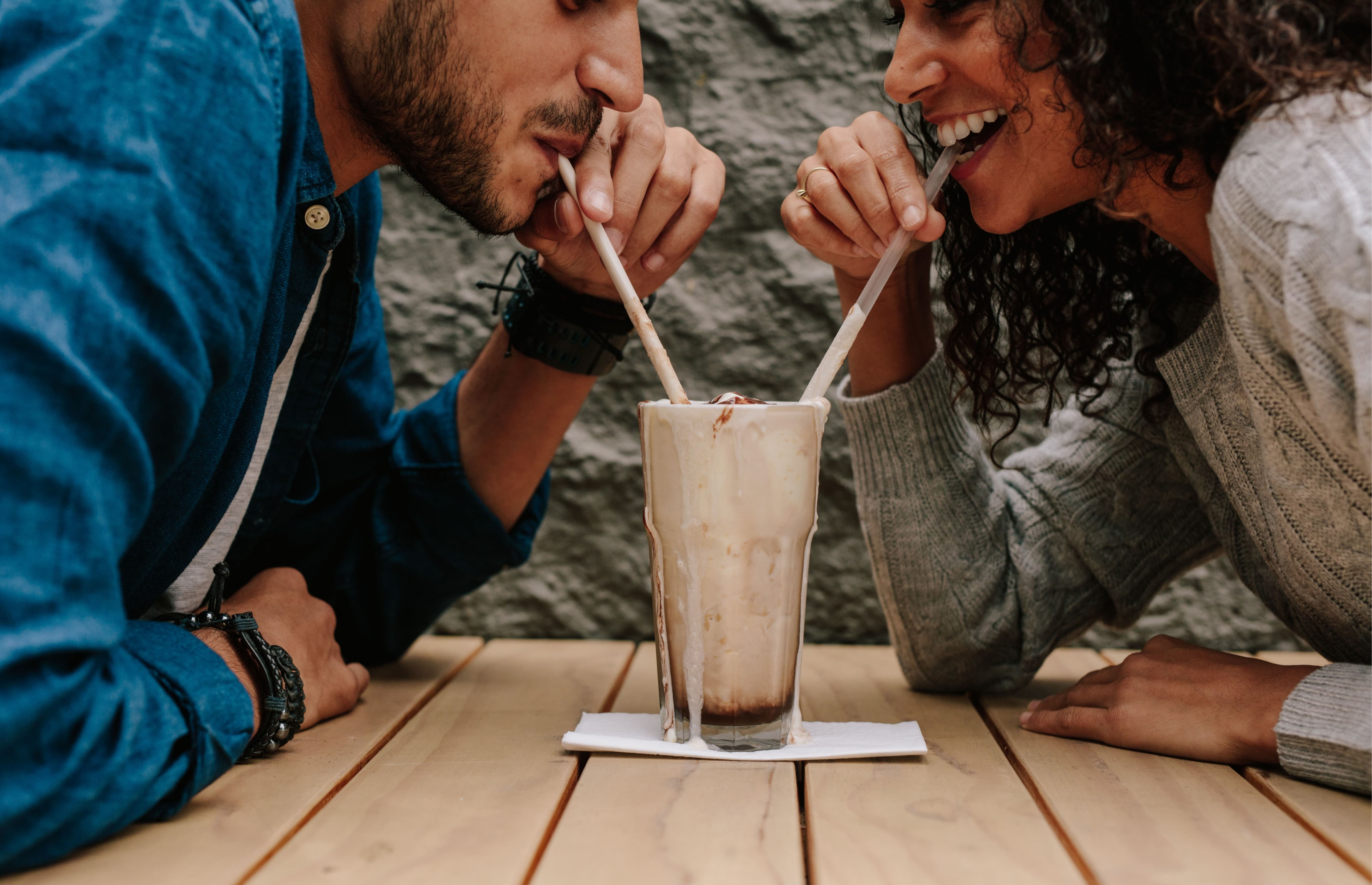 Smiling young couple sharing one chocolate milkshake with two straws, capturing the warmth of a friends to lovers relationship