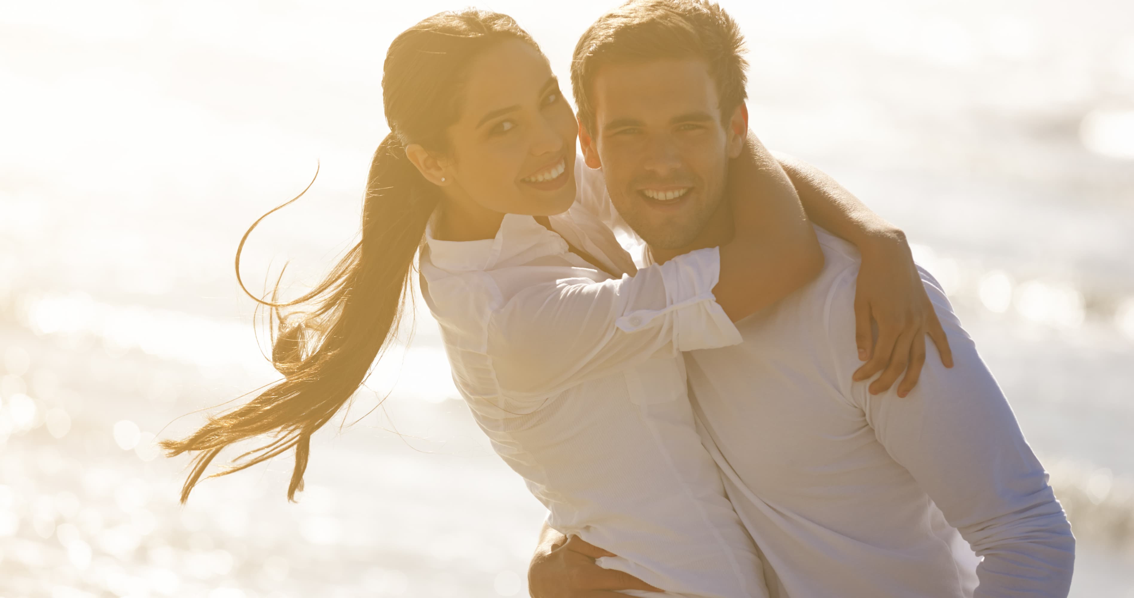 Romantic couple hugging and smiling together on a bright beach during golden hour.