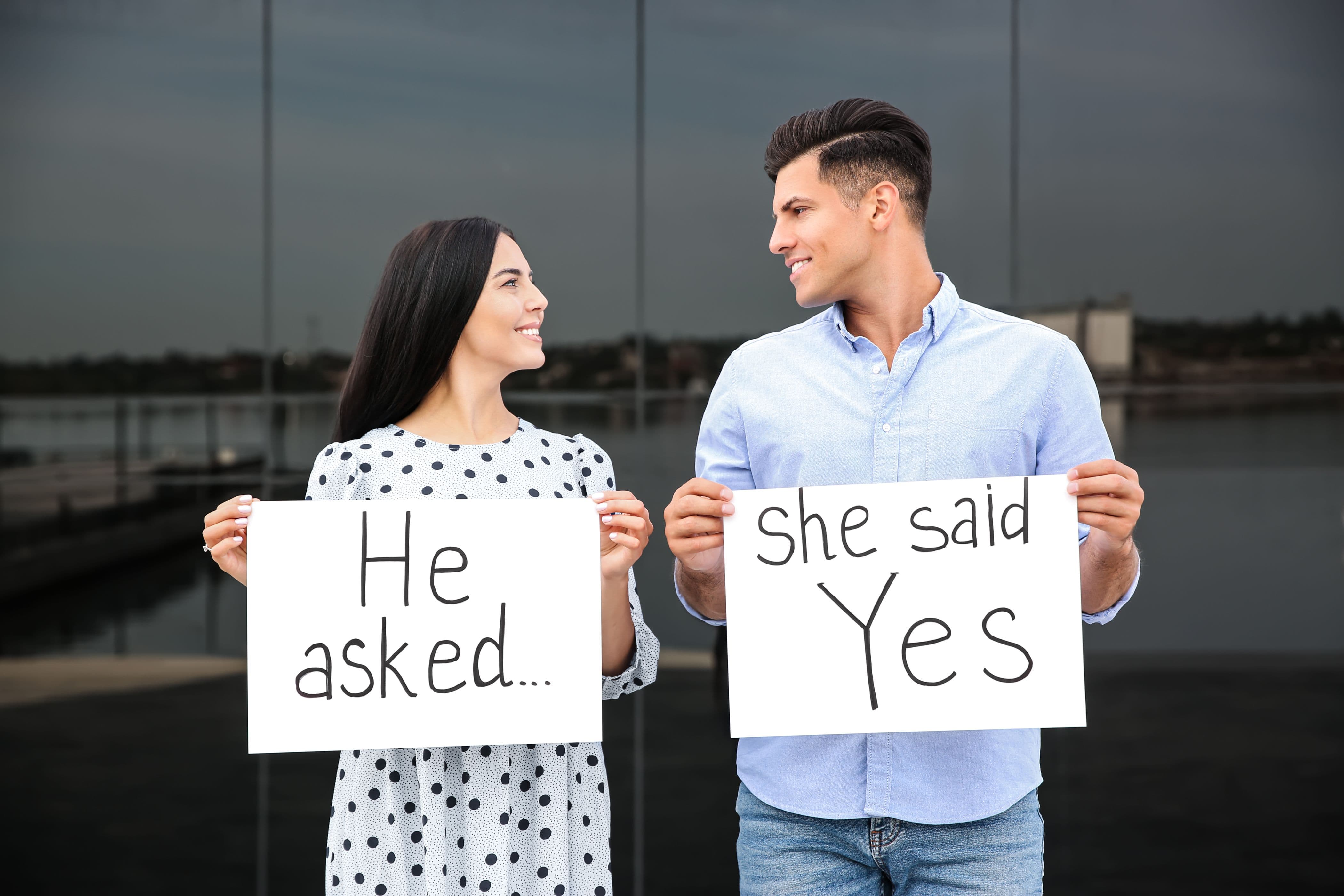 Man and woman smiling at each other while holding engagement announcement signs